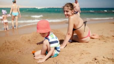 3 yaşındaki küçük oğluyla sahilde oynayan güzel genç annenin 4k yavaş çekim görüntüleri. Denizde dinlenen aile