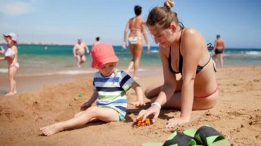 3 yaşındaki küçük oğluyla sahilde oynayan güzel genç annenin 4k yavaş çekim görüntüleri. Denizde dinlenen aile