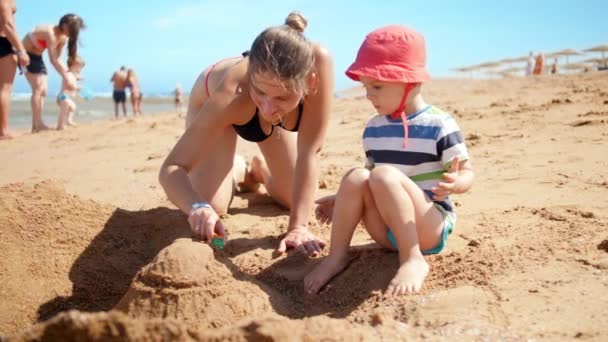 4k slow motion vídeo of cheerful little boy with smiling mother playing on sandy beach at sunny summer day — Vídeo de Stock