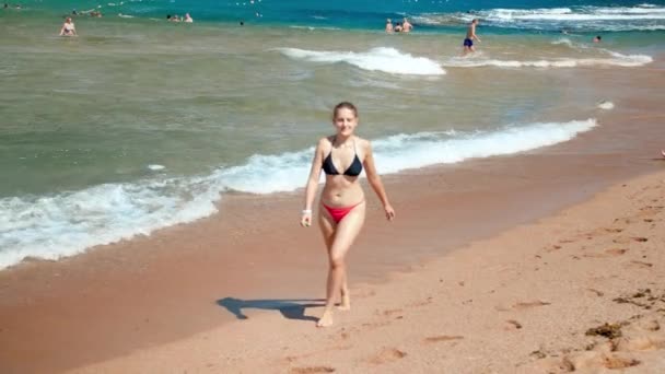 4k slow motion vídeo of beautiful young woman in bikini walking out of the sea on sandy beach — Vídeo de Stock