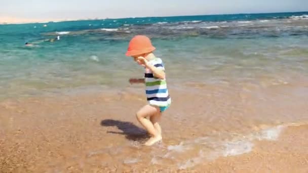 Imágenes de 4k del alegre niño riéndose jugando en olas marinas en la playa — Vídeo de stock