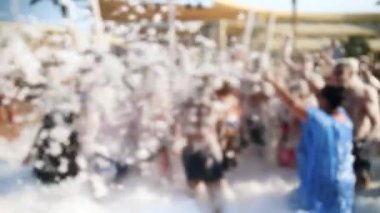 Parlak güneşli bir günde plajda dans mayo ve bikini neşeli kalabalık 4k video. Sabun köpüğü partisi olan gençler