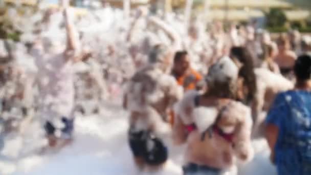 4k fuera de foco de vídeo de la multitud feliz cubierto de espuma de jabón bailando en la discoteca playa. Jóvenes disfrutando de vacaciones y relajarse en el caluroso día de verano — Vídeos de Stock