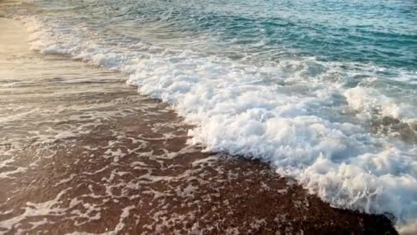 Gros plan vidéo au ralenti de tourbillonnant et bouillonnant l'eau de mer après les vagues écrasant sur le rivage au coucher du soleil — Video