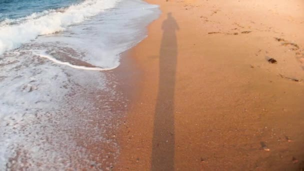 Αργή κίνηση σημείο των βίντεο από το άτομο που περπατάει στην αμμώδη παραλία στο ηλιοβασίλεμα — Αρχείο Βίντεο
