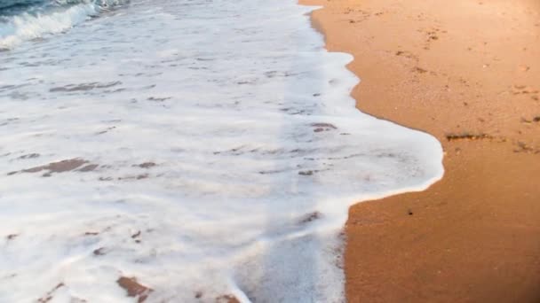 Närbild slow motion video av person som går längs havet vågor rullande på sandstranden vid solnedgången — Stockvideo