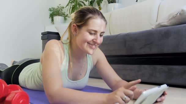 4k video of young woman exercising on floor a thome. She is watching how to do exercises oand stretching on tablet computer — Stock Video