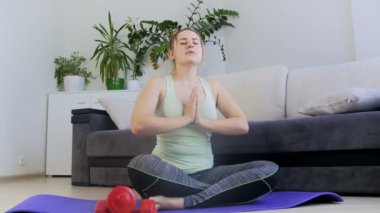 Evde yoga minderinde oturan ve meditasyon güzel genç kadın 4k görüntüleri