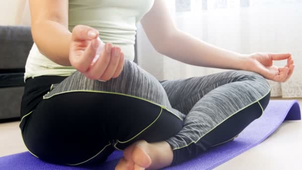 Oturma odasında fitness mat üzerinde lotus yoga pozisyonu oturan beautoful genç kadın Dolly 4k görüntüleri ve meditasyon — Stok video