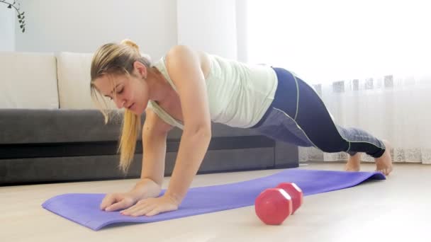 4k-beelden van jonge vrouwen die op de vloer vallen na het doen van beplanking en push-ups thuis — Stockvideo