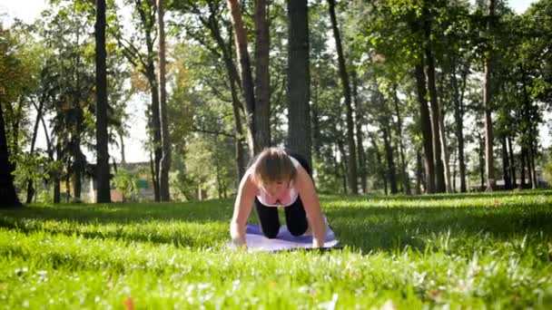 4K slow motion-bilder från mitten av den gamla leende kvinnan som tränar yoga i den offentliga parken på soliga sommardagar. Begreppet kropp och psykisk hälsa — Stockvideo