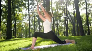 Parkta çim yoga 40s kadın 4k yavaş çekim video. Yetişkin bayan ormanda mat fitness egzersizleri yapıyor.