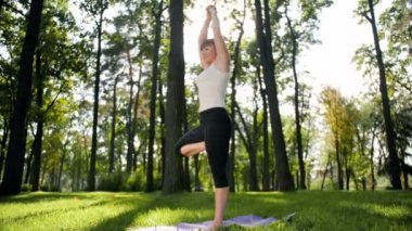 Parkta egzersiz orta yaşlı kadın 4k görüntüleri. Ormanda fitnes mat yoga yetişkin kadın pratik
