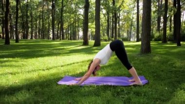 Parkta fitness mat üzerinde uzanan mutlu gülümseyen kadın 4k görüntüleri. Orta yaşlı bayan ormanda yoga egzersizleri yapıyor.