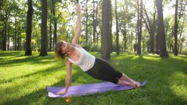 Güneşli yaz gününde kamu parkta yoga orta yaşlı gülümseyen kadın 4k yavaş çekim görüntüleri. Beden ve ruh sağlığı kavramı