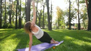 Yerel parkta mat fitness egzersizleri yapan 40 yaşındaki kadının 4k görüntüleri. Doğada zihinsel ve fiziksel sağlıklarıyla ilgi çeken insanlar
