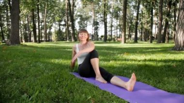 Yoga egzersizleri yapıyor ve parkta germe güzel gülümseyen orta yaşlı kadın 4k yavaş hareket video. Bu zihinsel ve fiziksel sağlık için çok yararlıdır. Doğada dinlenen insanlar