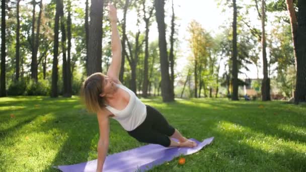 4K bilder av 40 år gammal kvinna gör Fitness övningar på mattan i lokal Park. Människor som tar hand om sin mentala och fysiska hälsa ute i naturen — Stockvideo