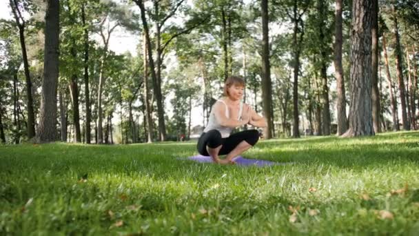4k felvétel a 40 éves nőt csinál fitness gyakorlatokat mat a helyi parkban. Emberek vigyáz a mentális és fizikai egészséget a természetben — Stock videók