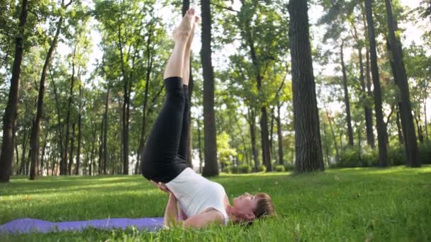 4k Zeitlupenvideo einer lächelnden Frau mittleren Alters, die an sonnigen Sommertagen im Park Yoga praktiziert und meditiert — Stockvideo