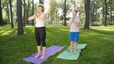 Parkta genç erkek yoga öğreten yetişkin kadının 4k yavaş çekim görüntüleri. Doğada fitness sınıfı egzersiz