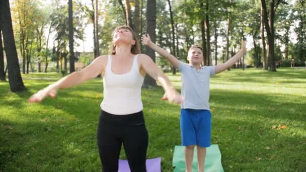 4k video of boy with adult woman doing yoga and fitness exercises in park. Parent teaching child taking care of health — Stock Video