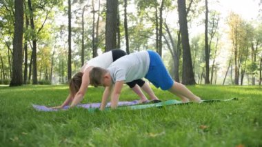 Parkta egzersiz anne ile çocuk yavaş hareket 4k görüntüleri. Aile yoga yapıyor ve doğada germe. Ciddi ve fiziksel bakım. Doğada uyum