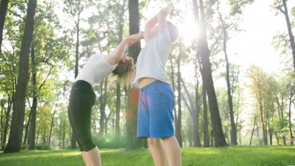 Des images au ralenti 4k montrant un garçon faisant des exercices de yoga sur l'herbe au parc avec sa mère. Femme enseignant à un enfant en cours de fitness — Video