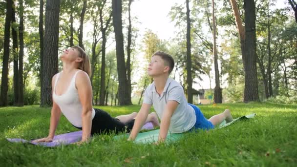 4k视频的男孩与成年妇女做瑜伽和健身锻炼在公园。家长教导儿童照顾健康 — 图库视频影像