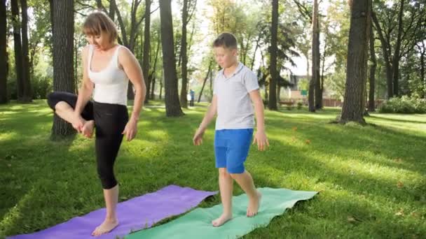 4k video en cámara lenta de mujer de mediana edad enseñando haciendo ejercicios y asana en clase de yoga en el parque — Vídeo de stock