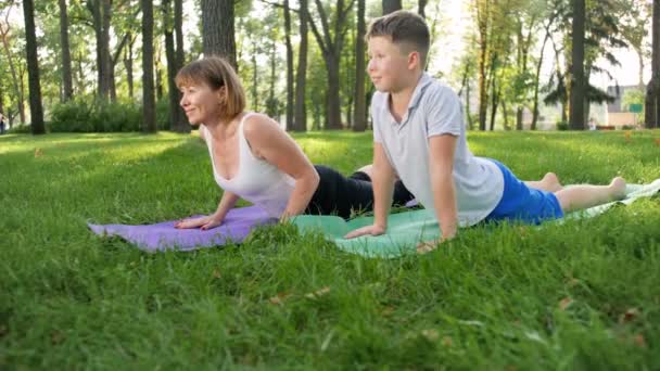 4k slow motion footage of adult woman teaching teenage boy yoga in park. Fitness class exercising in nature — Stock Video