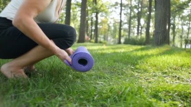 Parkta yoga egzersizleri için fitness minderi atan ve atan kadının yavaş çekim yakın çekim videosu