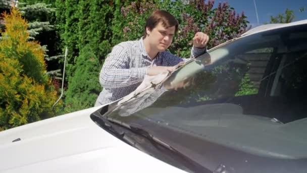 家の裏庭で彼の車の窓や窓を掃除する男性運転手の4k映像。個人の車の世話をする — ストック動画