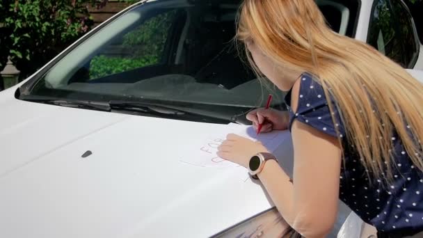 Zeitlupenvideo einer jungen Frau, die ein Verkaufsschild auf das Blatt Papier schreibt und es unter den Scheibenwischer ihres alten Autos legt — Stockvideo
