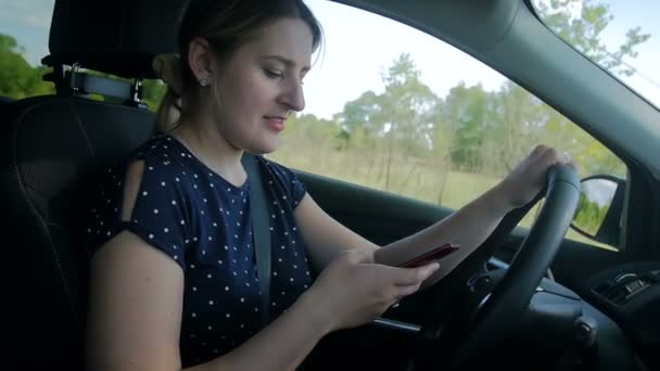 Filmagem em câmera lenta de uma jovem usando smartphone enquanto dirige um carro. Por favor, use as mãos livres no veículo para sua segurança — Vídeo de Stock