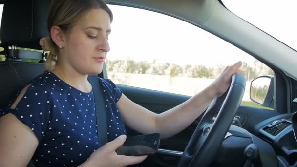 Imágenes en cámara lenta de una mujer joven usando un teléfono inteligente mientras conduce un coche. Por favor, utilice manos libres en el vehículo para su seguridad — Vídeos de Stock