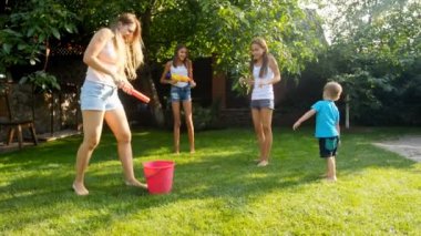 Su tabancaları ve bahçe hortumu ile bahçede eğlenen mutlu neşeli aile yavaş hareket görüntüleri. Birbirlerine su sıçratan