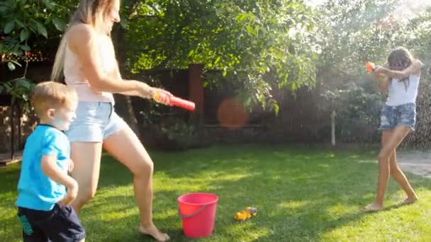 Zeitlupenaufnahmen von Kindern, die an heißen Sommertagen mit Wasserpistolen und Gartenschlauch spielen. alle Kleider werden nass — Stockvideo