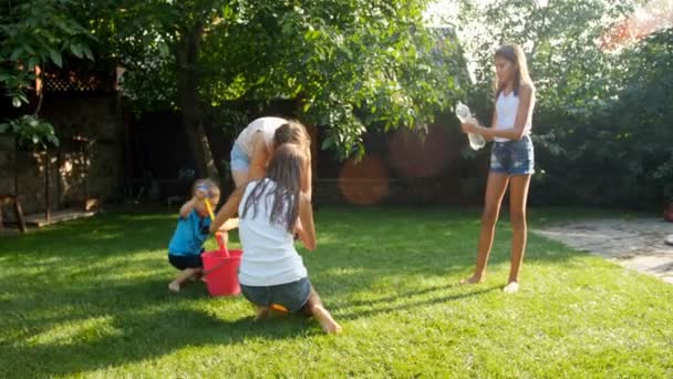 4k filmato di felici adolescenti allegri che giocano in giardino con pistole ad acqua e spruzzi d'acqua l'uno sull'altro — Video Stock