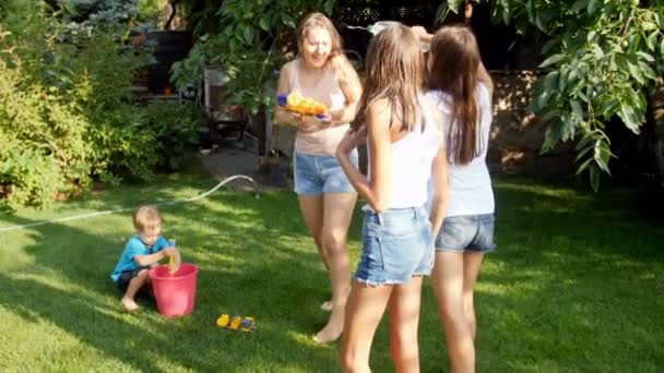 Video al rallentatore di allegra giovane famiglia con bambini che giocano con pistole ad acqua e tubo dell'acqua in giardino durante la calda giornata estiva — Video Stock