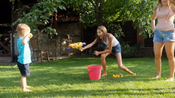 暑い夏の日に水銃と庭のホースで遊ぶ子供たちのスローモーション映像。すべての服が濡れる — ストック動画