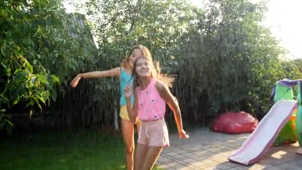 Vídeo em câmera lenta de duas adolescentes alegres dançando sob a chuva de verão sob a luz do pôr do sol — Vídeo de Stock