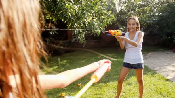Images au ralenti d'une famille heureuse et joyeuse qui s'amuse dans le jardin avec des pistolets à eau et un tuyau d'arrosage. Éclaboussures d'eau l'un sur l'autre — Video