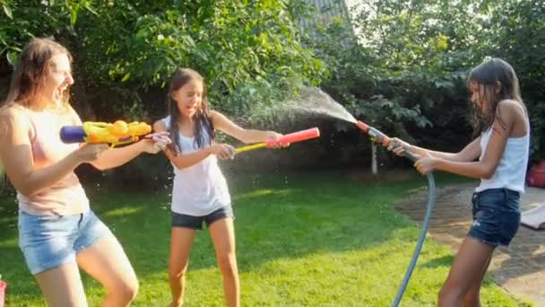 Медленная съемка счастливой веселой семьи, развлекающейся в саду с водяными пистолетами и садовым шлангом. Разбрызгивая воду друг на друга — стоковое видео