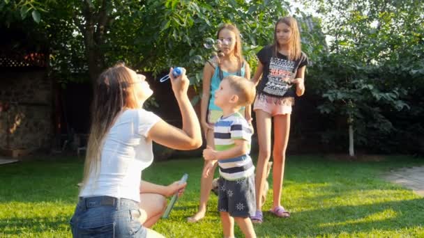 4k video of cheerful laughing children catching soap bubbles that mother is blowing in park — Stock Video