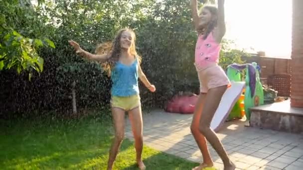 Pomalý film z veselých dospívajících dívek tančících a skákající se zahradní hadičkou za horkého letního dne — Stock video