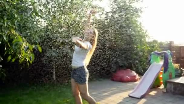 Повільний рух кадрів щасливої усміхненої молодої жінки в білій футболці танцює і стрибає під теплим літнім дощем на заході сонця — стокове відео
