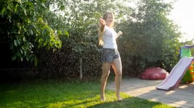 Arka bahçesinde bahçe hortumu su altında dans uzun saçlı cherful genç kadının Yavaş hareket video