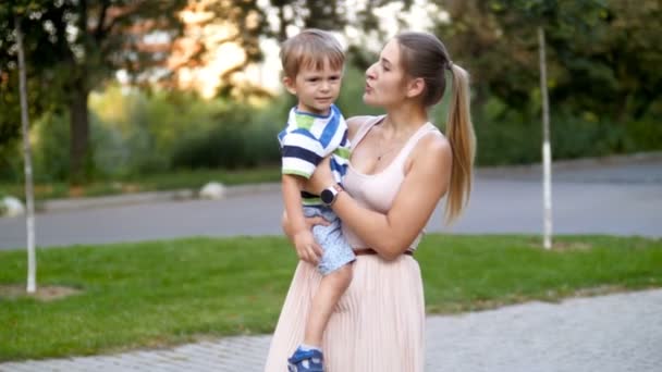 4k filmagem de jovem mãe segurando abraçando seu menino e andando no parque — Vídeo de Stock