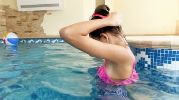 4k видео улыбающейся девочки в очках для дайвинга и плавания под водой в крытом бассейне в тренажерном зале — стоковое видео